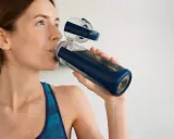 Kobieta w sportowym topie pije wodę z butelki. Dbanie o nawodnienie i elektrolity co to jest ważne dla regeneracji.
