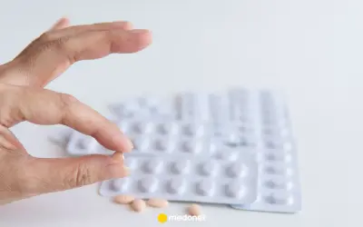 Szukasz co zamiast statyn na cholesterol? Dłoń trzyma tabletkę, w tle blistry leków.