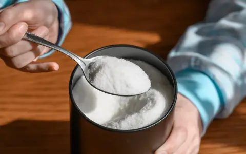 Łyżka białego proszku, z którego produkowany jest erytrytol, nad stołem.