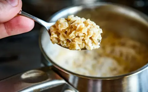 Łyżka gotowanych płatków owsianych, które pomagają obniżyć cholesterol. W tle garnek z owsianką.