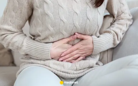 Kobieta trzyma się za brzuch, odczuwając ból brzucha po jedzeniu.