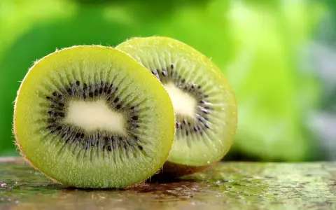 Dwa soczyste kiwi, przekrojone na pół, ukazują swoje zielone wnętrze z czarnymi pestkami. To naturalne kiwi co leczy, pełne witamin.