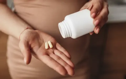 Dłoń z dwiema kapsułkami, obok biała buteleczka. Probiotyki przy antykoncepcji mogą wspierać równowagę organizmu.