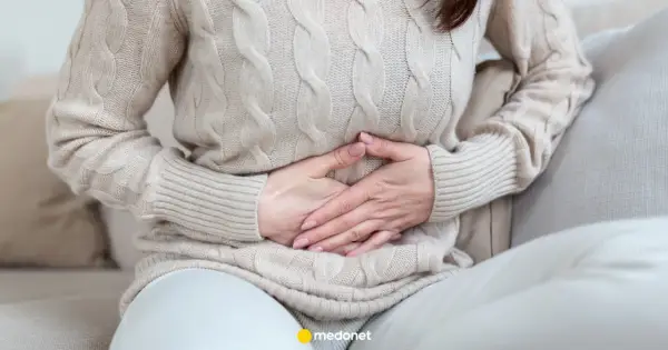 Kobieta trzyma się za brzuch, odczuwając ból brzucha po jedzeniu.