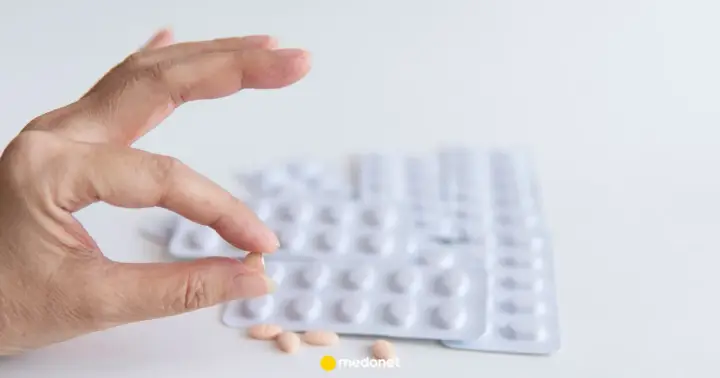 Szukasz co zamiast statyn na cholesterol? Dłoń trzyma tabletkę, w tle blistry leków.